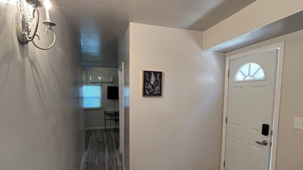 Un couloir avec une chaise blanche, une porte dotée d’une fenêtre et un luminaire fixé au mur.