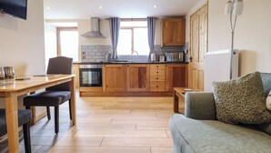 Eine moderne Küche mit Holzschränken, ein Essbereich mit Tisch und Stühlen sowie ein Wohnzimmer mit Sofa und Lampe.