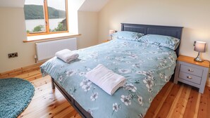 Ein Schlafzimmer mit einem Bett, einem Nachttisch, einem Fenster mit Seeblick und Holzboden.