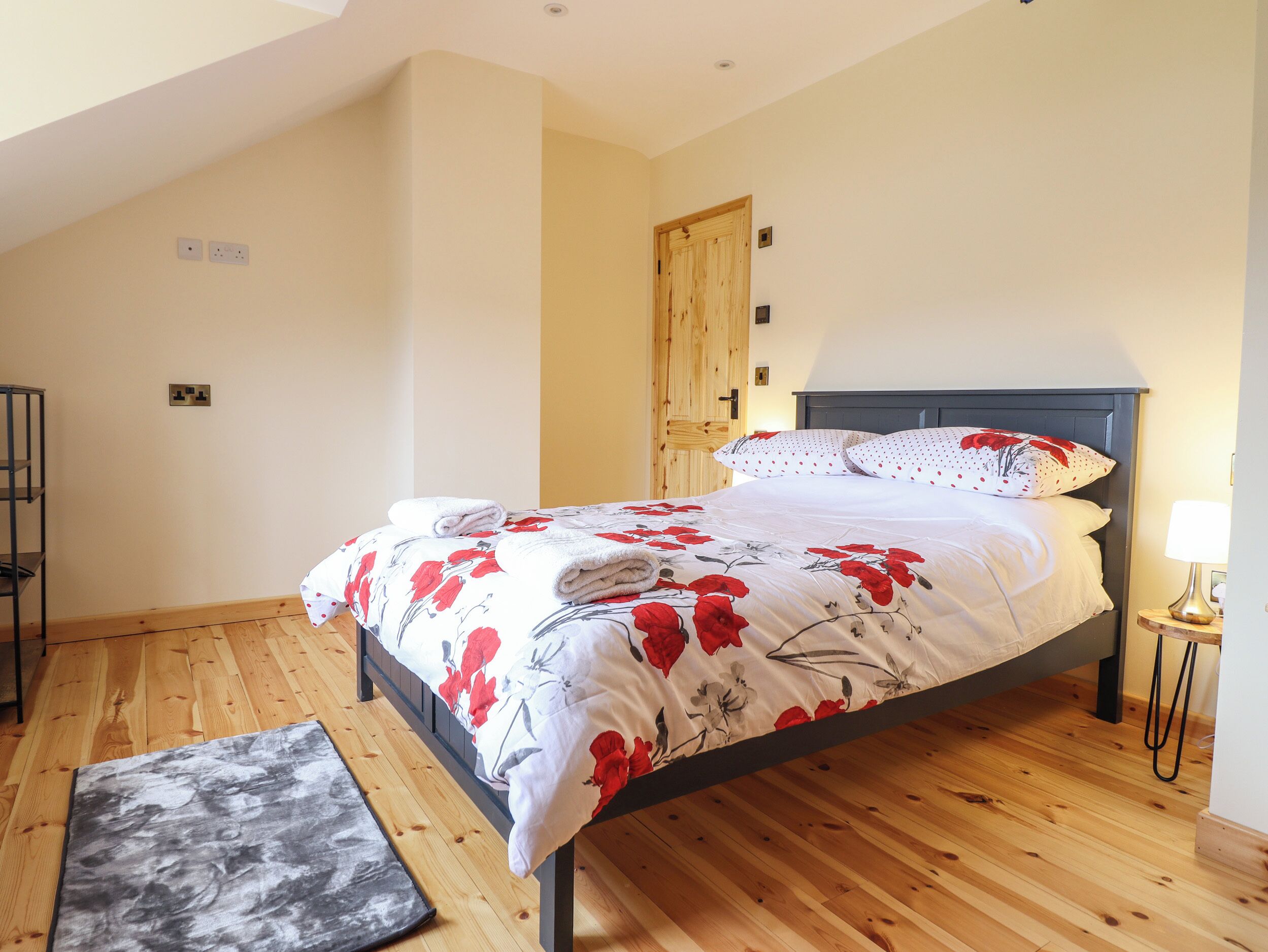 Een slaapkamer met een bed, een houten vloer, een deur en een nachtkastje met een lamp.