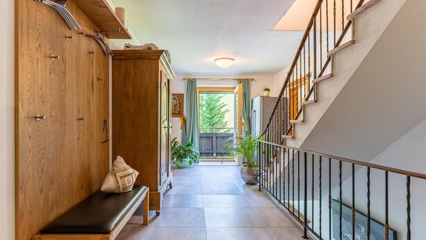 Un pasillo con un banco de madera, una escalera y vistas al exterior.