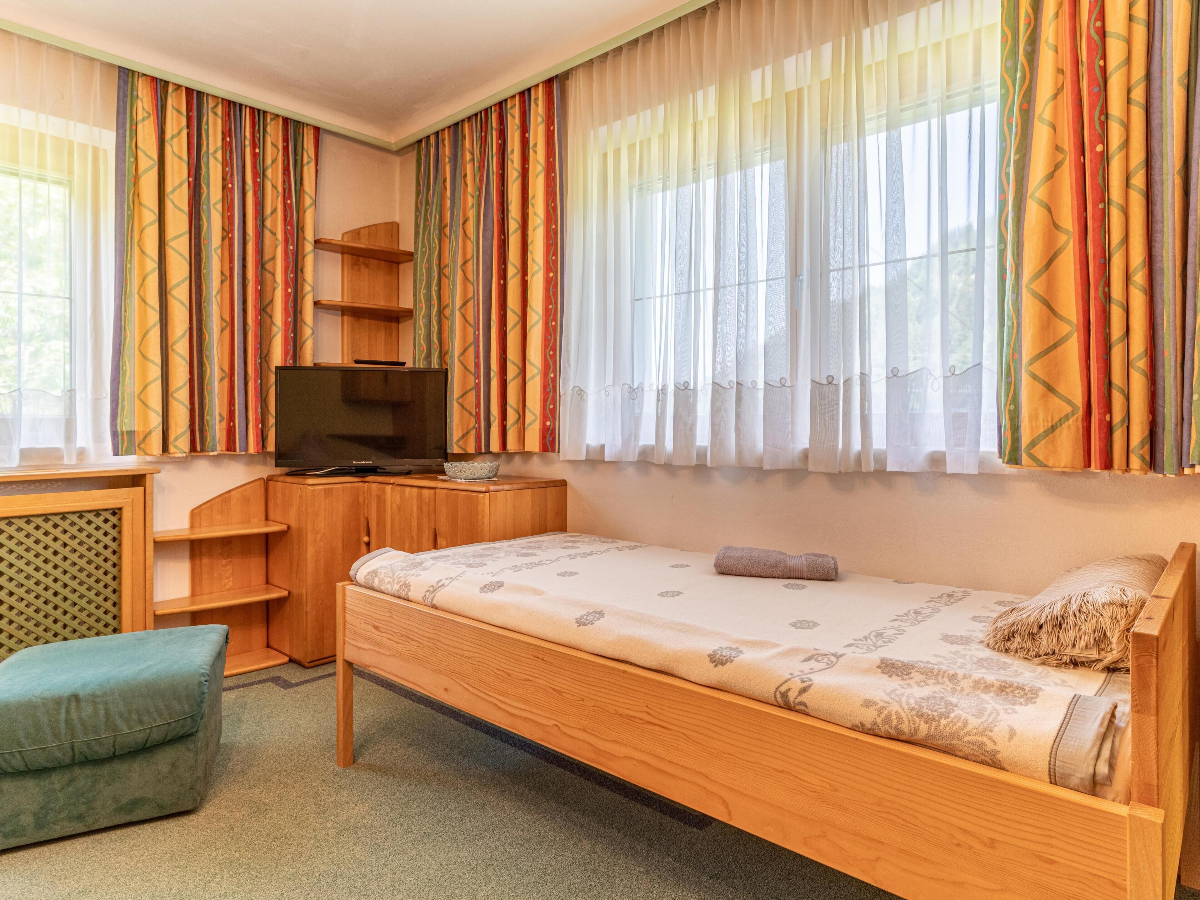 A bedroom with a wooden bed, a desk with a television, and colorful curtains.