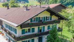 Un edificio de varios pisos con techo inclinado, balcones con macetas de flores y un jardín bien cuidado.