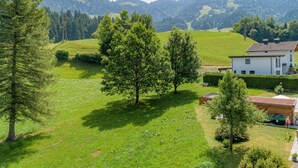 Una casa rural con jardín, rodeada de árboles y colinas.