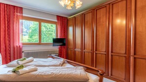 Un dormitorio con una cama grande, un armario de madera, televisor y ventana con cortinas.