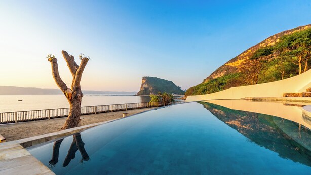 A infinity pool with a clear view of the sea and a mountain in the background. - Inlight Lombok Eco Resort (Kuta)