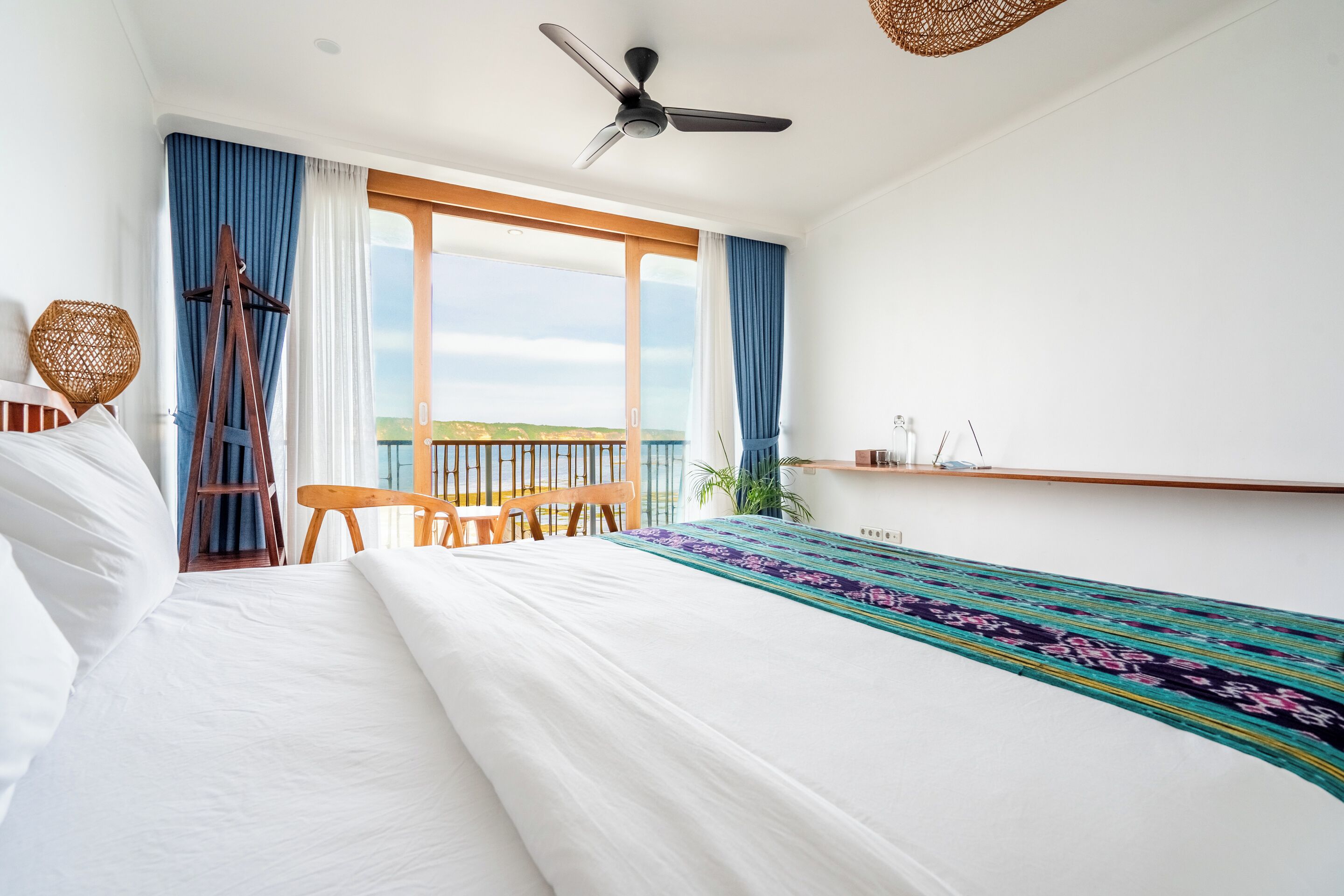 Habitación de hotel con una cama grande, un escritorio, una silla, un ventilador de techo y vistas al exterior.