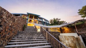 A staircase leading to a modern building with a stone wall on one side and a metal railing on the other. - Inlight Lombok Eco Resort (Kuta)