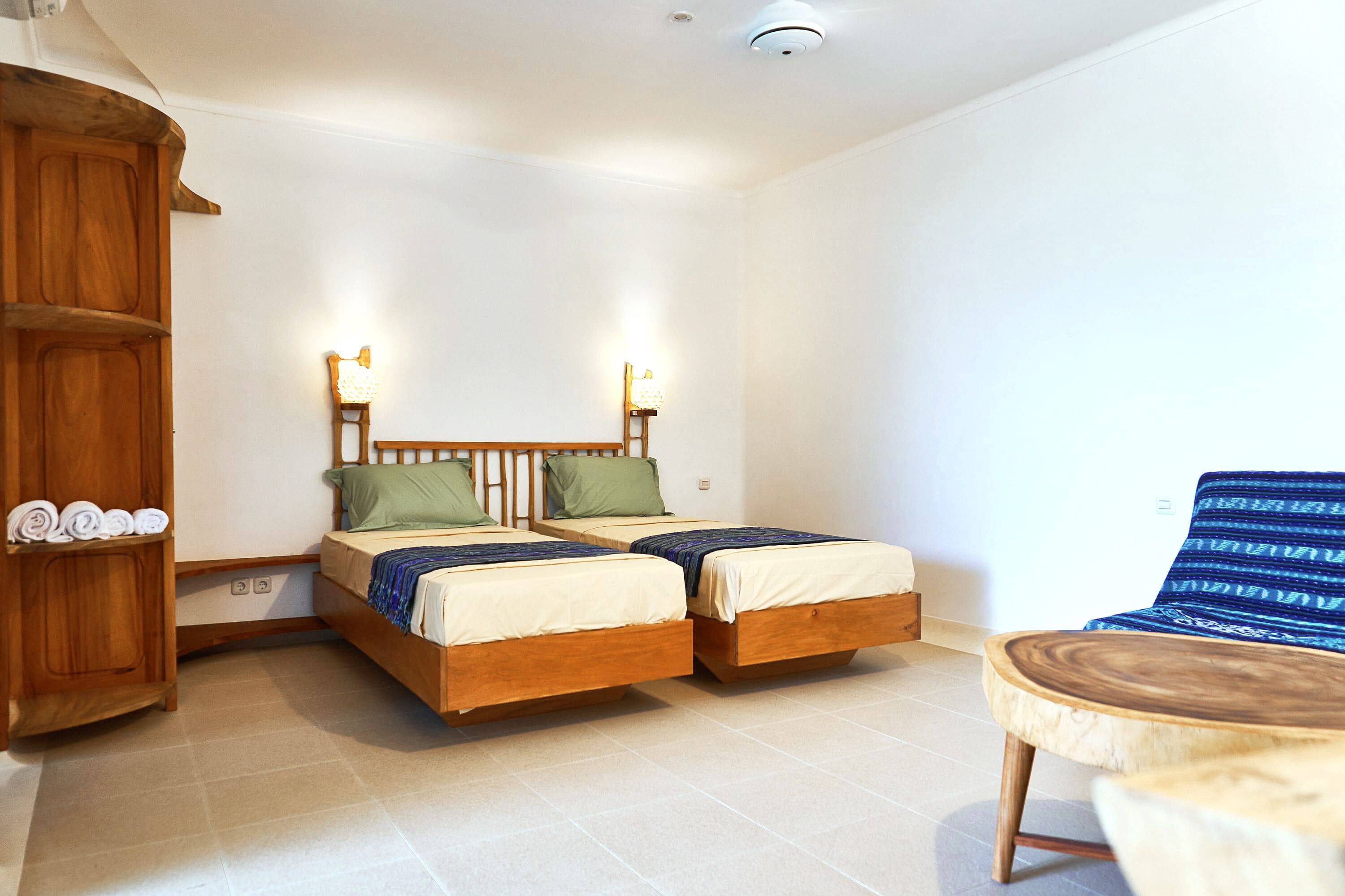 Une pièce comprenant deux lits en bois, une armoire en bois, une table ronde en bois et une chaise à rayures bleues.