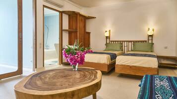 Habitación de hotel con dos camas, una mesita de madera, un florero con flores y vistas al exterior.