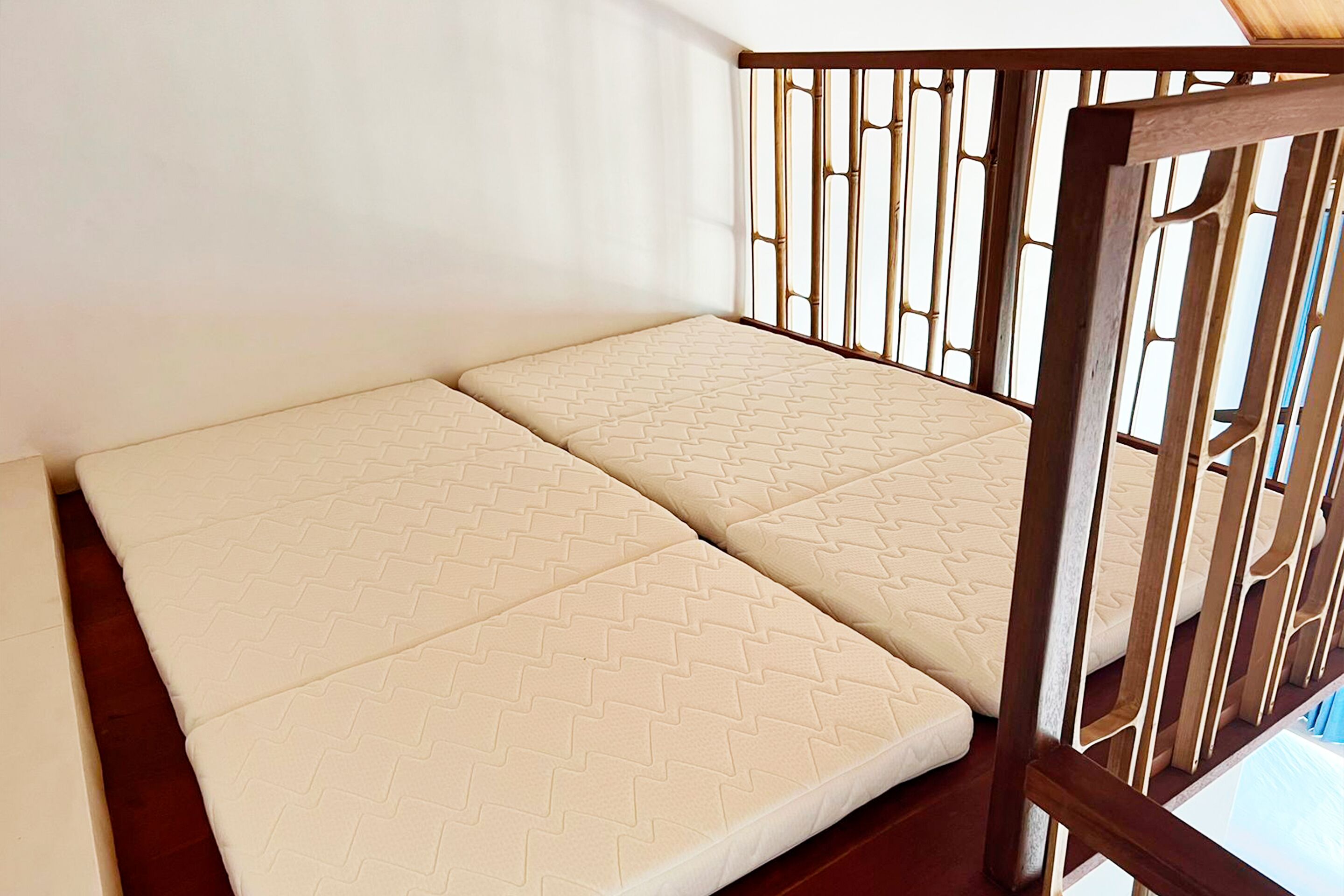 A room with a bed against a wall, a wooden railing, and a window.