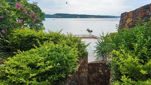 A view of a coastal area with a stone bridge, lush greenery, and a calm sea. - Inlight Lombok Eco Resort (Kuta)