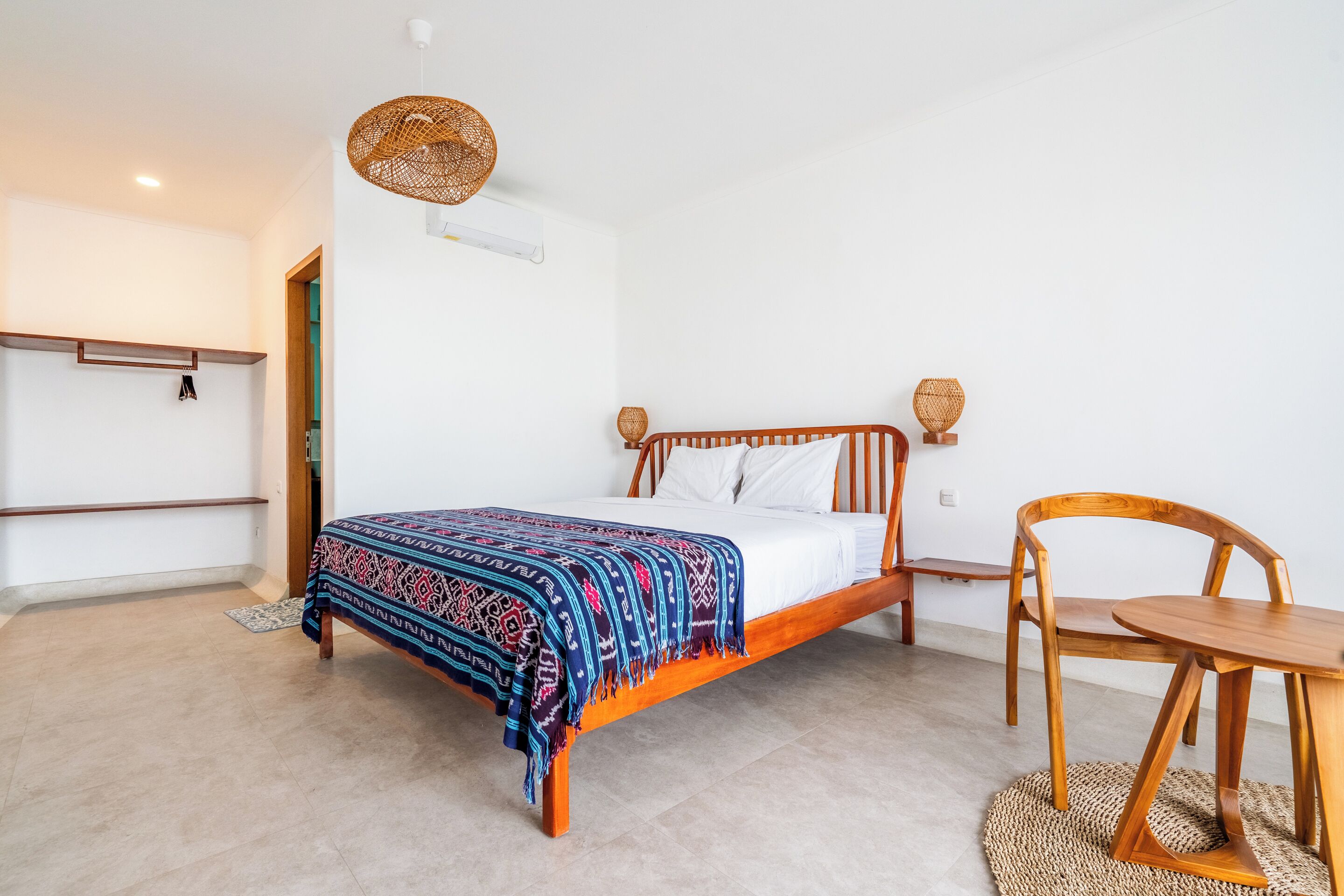 Quarto com cama de madeira, mesa de cabeceira, cadeira e luminária pendente.