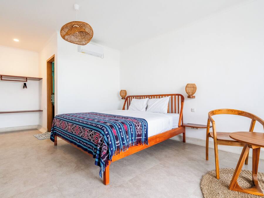 Quarto com cama de madeira, mesa de cabeceira, cadeira e luminária pendente.