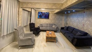 A living room with a grey sofa, a black armchair, and a wooden coffee table. A flat-screen TV is mounted on the wall. - Bona Sera Hotel (Istanbul)