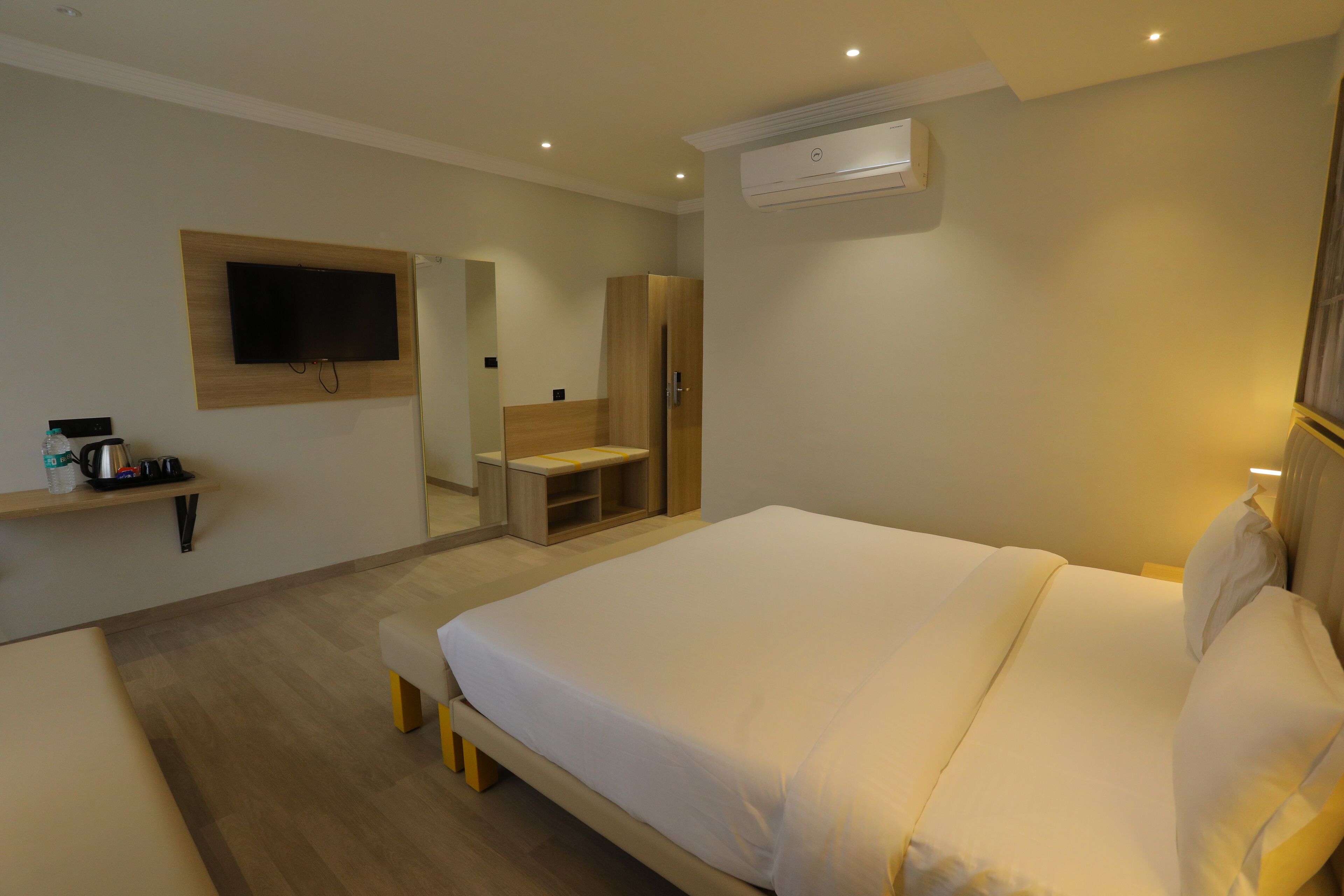Una habitación de hotel moderna con una cama grande, un televisor montado en la pared, un armario y un pequeño rincón de descanso.