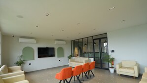 Un área de espera amplia con diversas opciones de asientos, incluyendo sillas y sofás, un televisor de pantalla plana en la pared y una planta en maceta.