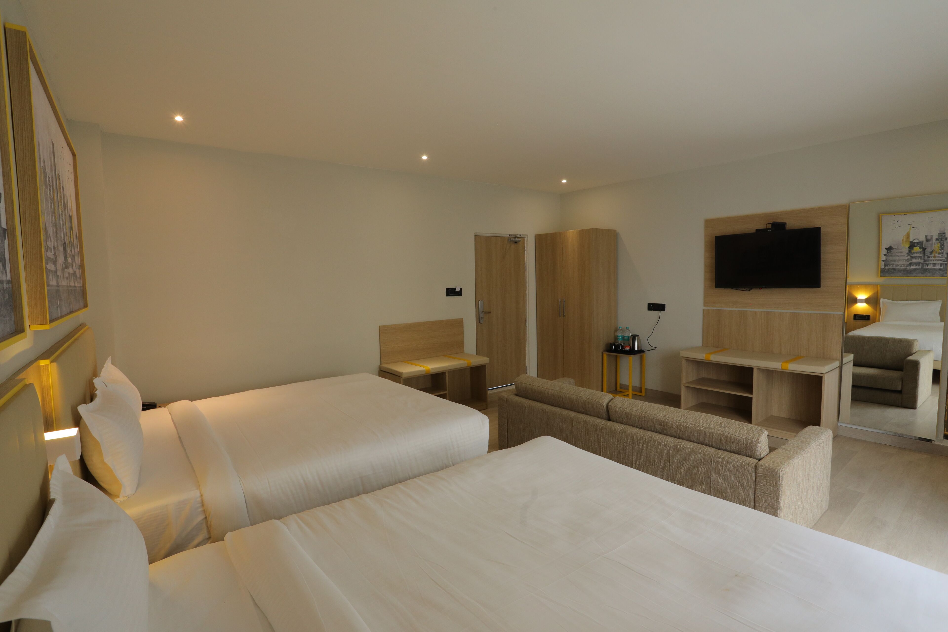 A hotel room with two beds, a sofa, a TV, and a desk with a chair.