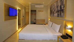 Habitación de hotel con una cama grande, televisión, un cuadro y una mesita de noche con lámpara.