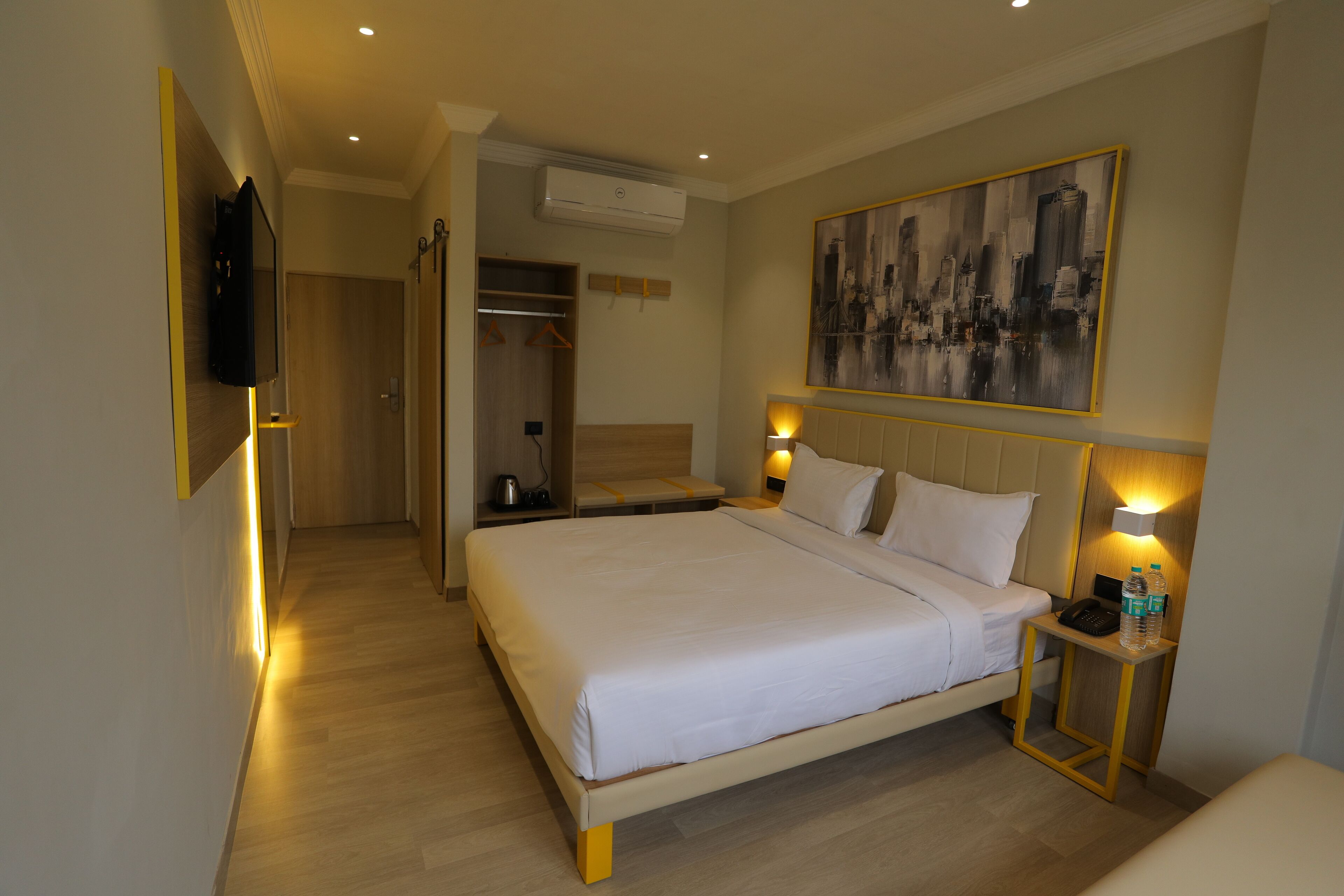 Hotelkamer met een bed, bedlampen, een schilderij aan de muur en een tafeltje met een telefoon en waterflesjes.