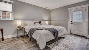 Un dormitorio con cama, mesitas de noche, una puerta y una ventana.