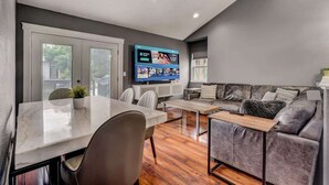 Una sala de estar moderna con comedor, un sofá gris, un televisor de pantalla plana y una mesa de centro de madera.