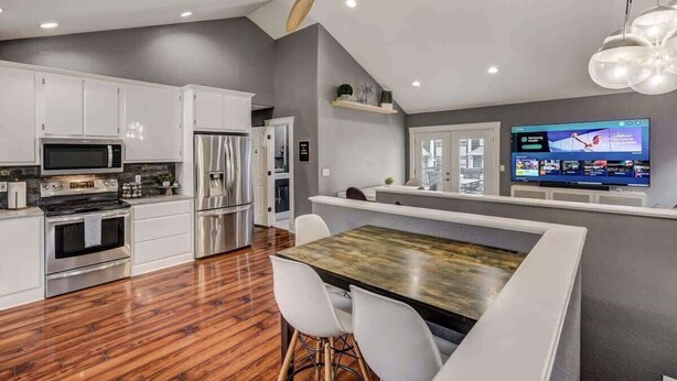 Una cocina moderna con armarios blancos, electrodomésticos de acero inoxidable y una mesa de comedor de madera con sillas blancas.