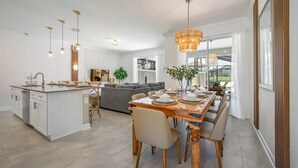 Een moderne keuken met een centraal eiland, een eethoek met een houten tafel en stoelen, en een woonkamer met een bank en een groot raam.