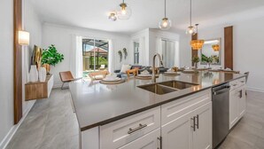 Een moderne keuken met een groot kookeiland, witte kasten en hanglampen.