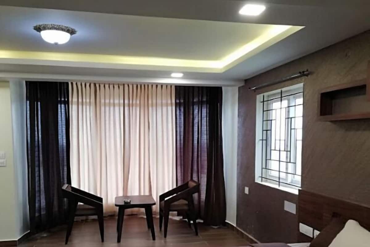 A hotel room with a bed, two chairs, a small table, a window with bars, and a ceiling light.
