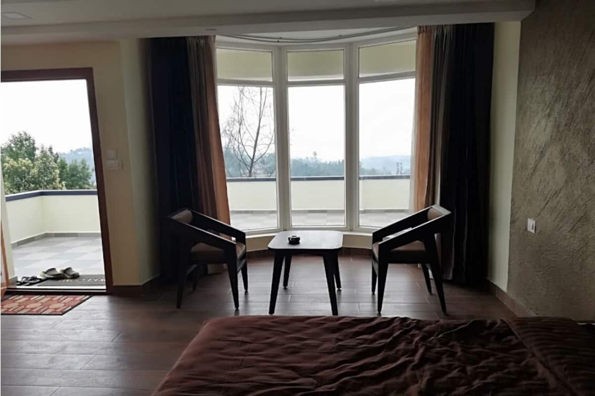 A hotel room with a large bed, a small table, two chairs, and a view through a large window.