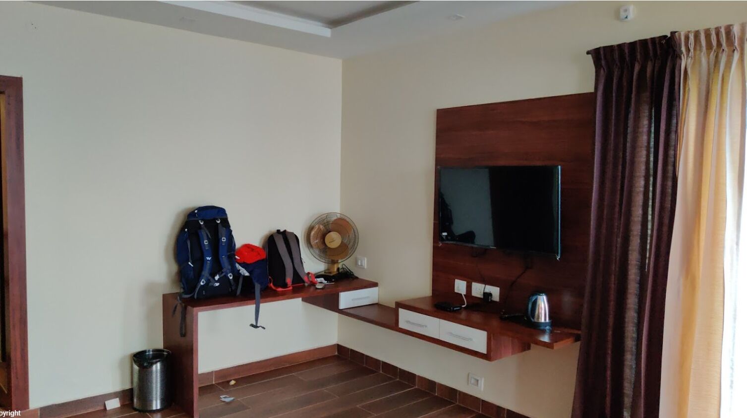 Ein Hotelzimmer mit Holzschreibtisch, Flachbildfernseher, Ventilator und Wasserkocher.