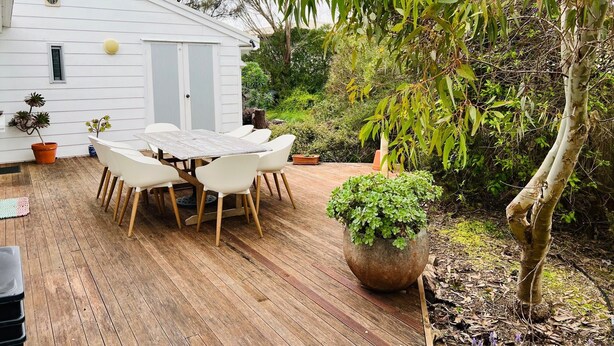 Una terraza de madera con una mesa y sillas, rodeada de macetas y árboles.