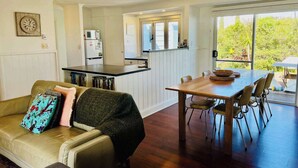 Una cocina moderna con armarios blancos, un comedor con mesa y sillas de madera, y un ventanal que ofrece vistas al verdor.