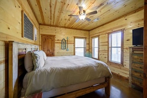 A wooden cabin bedroom with a bed, a ceiling fan, and a dresser. - Luxury Rustic Cabin • Hot Tub & Spa • Fire Pit (Broken Bow)