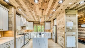 A modern kitchen with wooden walls, white cabinetry, and a marble island. - Laughing Pines - Indoor pool & theater room (Smoky Mountains)