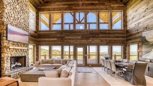 A spacious interior with a stone fireplace, a large sofa, a dining area, and large windows. - Laughing Pines - Indoor pool & theater room (Smoky Mountains)