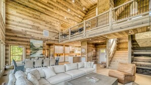 A spacious living area with a large sectional sofa, a coffee table, and a balcony with a railing. - Laughing Pines - Indoor pool & theater room (Smoky Mountains)