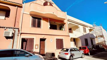 Un edificio a più piani con tetto piatto e un balcone al secondo piano, con ingresso a livello strada. Davanti all'edificio si vedono auto parcheggiate.