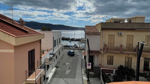 A narrow street with buildings on either side, a parked car, and a body of water in the distance under a cloudy sky. - Cirismiro Torre Faro B&B  (Torre Faro)