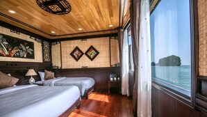 Een kamer met twee bedden, houten vloeren, een groot raam met uitzicht op zee en traditionele wanddecoratie.