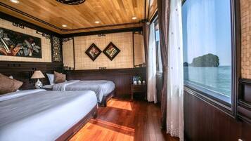 A room with two beds, wooden flooring, a large window with a view of the sea, and traditional wall decor.