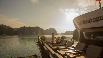 A balcony with lounge chairs overlooking a body of water and distant mountains.