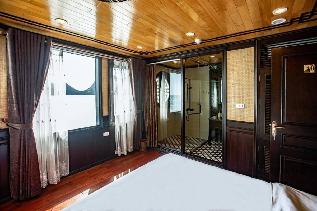 Habitación de hotel con techo de madera, una cama, una puerta corredera de vidrio que da al baño y vistas al exterior.