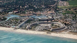 An aerial view of a coastal resort with a large circular building, a marina, and a beach.