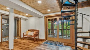 Una habitación amplia con suelo de madera, un banco de madera, una escalera de caracol y un gran ventanal que da a un balcón.