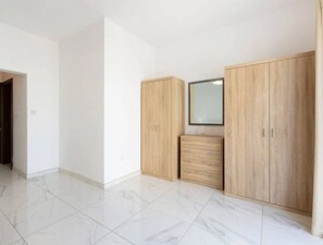 Een ruime kamer met een grote kast, een spiegel en een klein dressoir.
