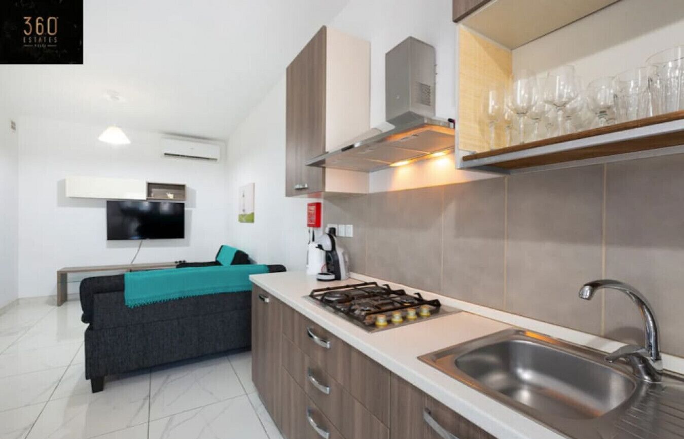 Eine moderne Küche mit Gasherd, Edelstahlspüle und einem flachbildfernseher an der Wand.