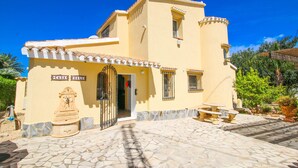A two-story building with a tiled roof, a stone-paved entrance, and a statue outside. - Villa with private pool in Denia (Denia)