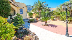 A courtyard with a paved walkway, palm trees, and a building with a blue window. - Villa with private pool in Denia (Denia)